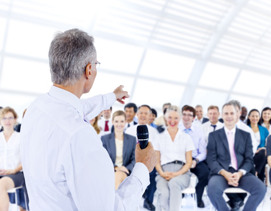 male speaker pointing at group of business people